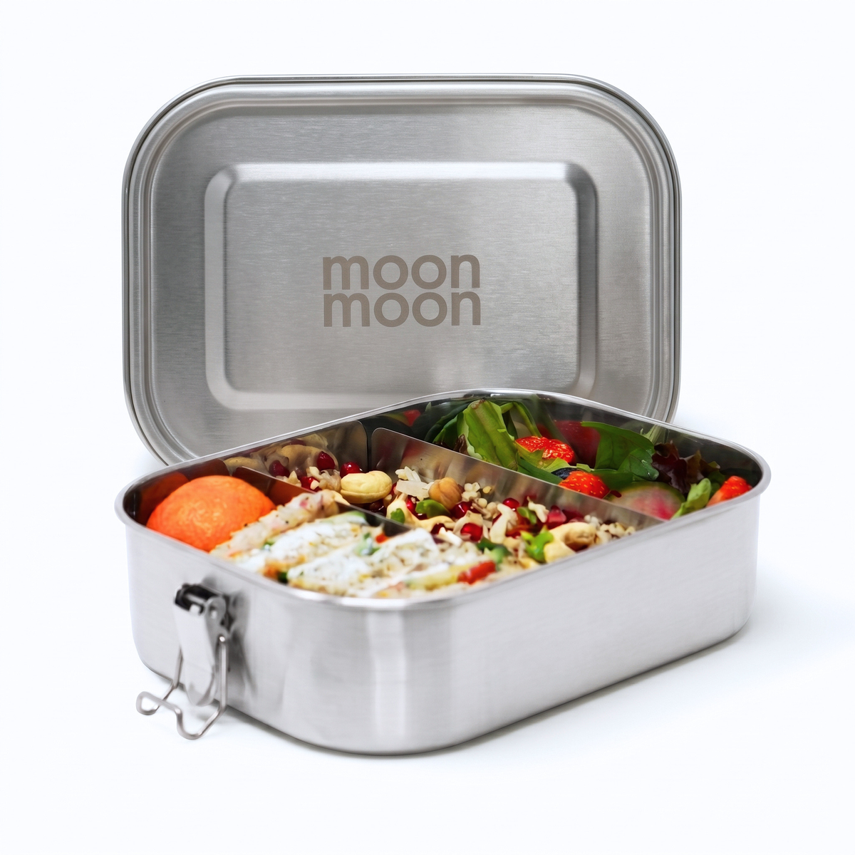 A large moonmoon stainless steel lunch box with its lid propped open, showing a divided tray filled with a colorful salad, crackers, and fruit. The inside of the lid is brushed silver with moonmoon printed on the lid.