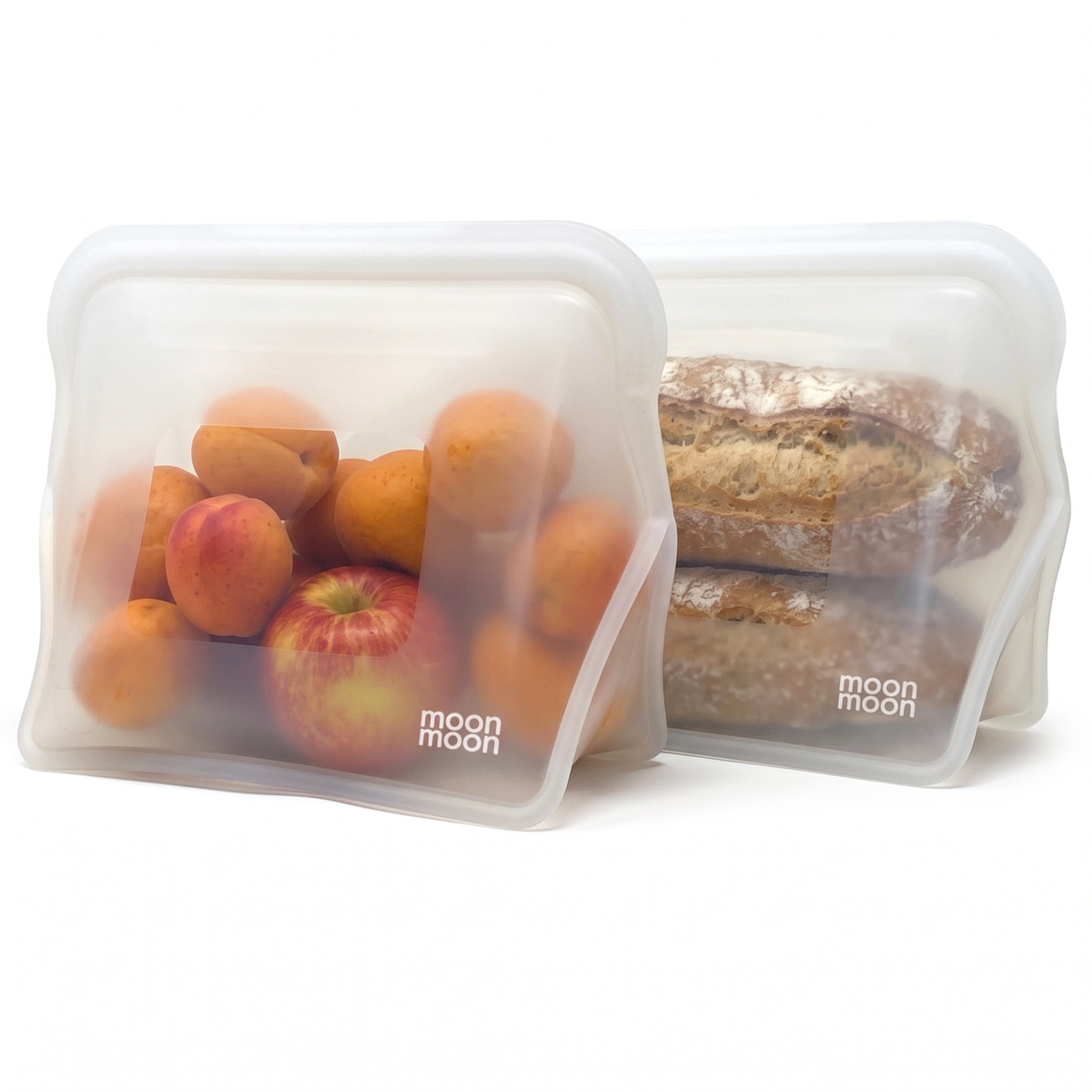 Two translucent moonmoon reusable silicone food bags with wide stand-up bases and pinch seals, shown on a white background. The front bag contains oranges and a red apple, and the back bag contains sliced bread.