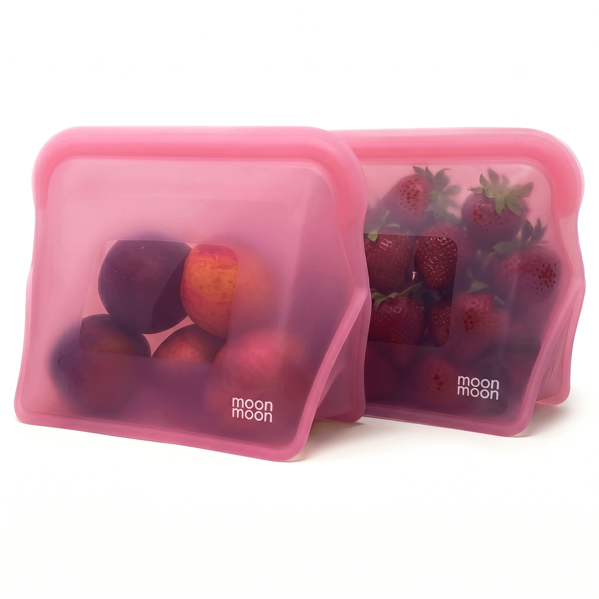 Two moonmoon reusable silicone food storage bags with wide stand-up bases and rounded corners. The bags have a translucent pink colour and are filled with fresh fruit.
