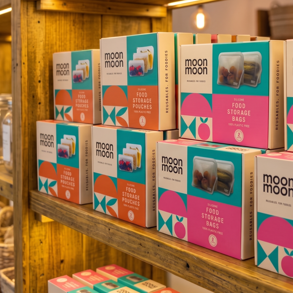 Moon Moon branded boxes of reusable food storage pouches and food storage bags displayed on wooden shelves in a retail setting.